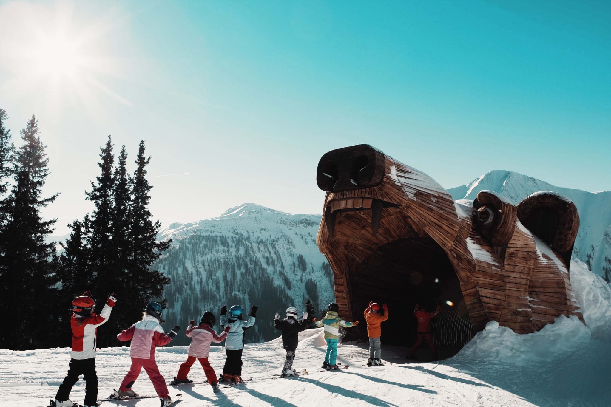 7 Kinder fahren mit den Ski in einen Holzbären hinein