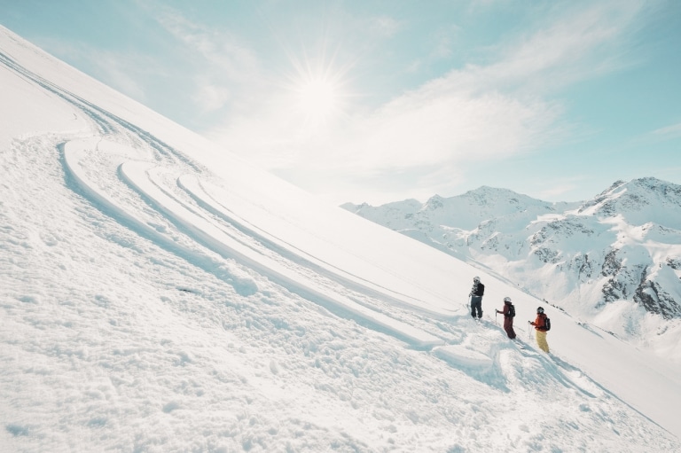 3 Skifahrer stehen mitten auf Piste und genießen die strahlende Sonne
