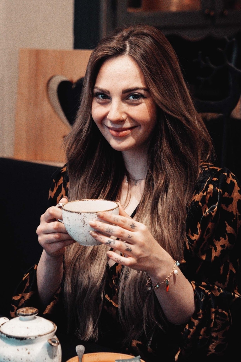 Junge Frau lächelt mit Tasse Tee in der Hand freundlich in die Kamera
