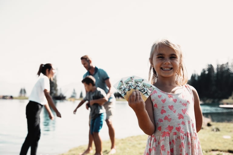 Mädchen hält Karten in der Hand während restliche Familie im Hintergrund tobt