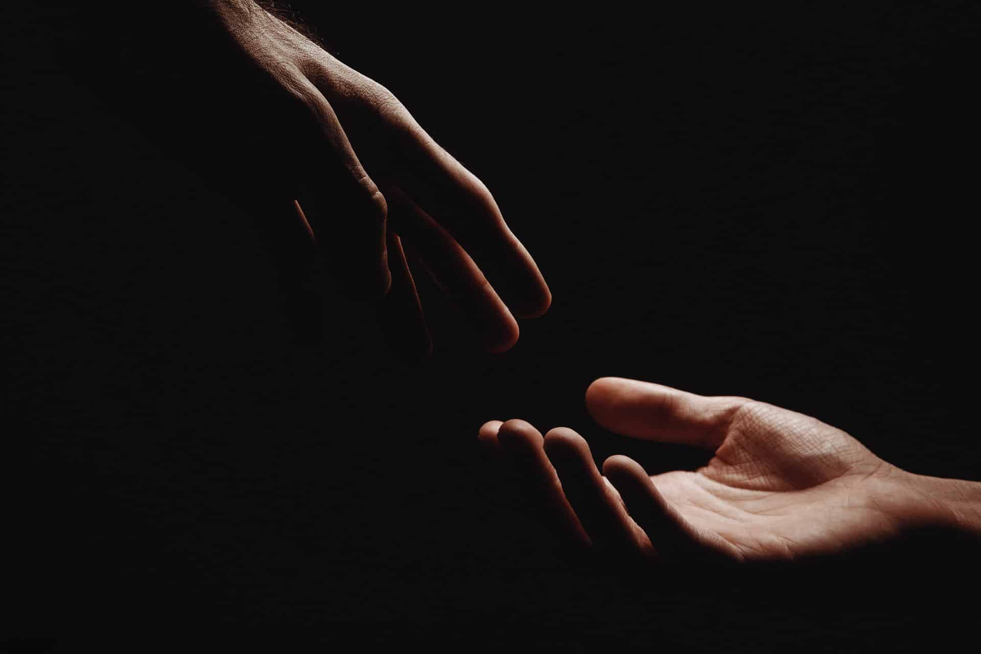 2 Hände berühren sich fast in Dunkelheit